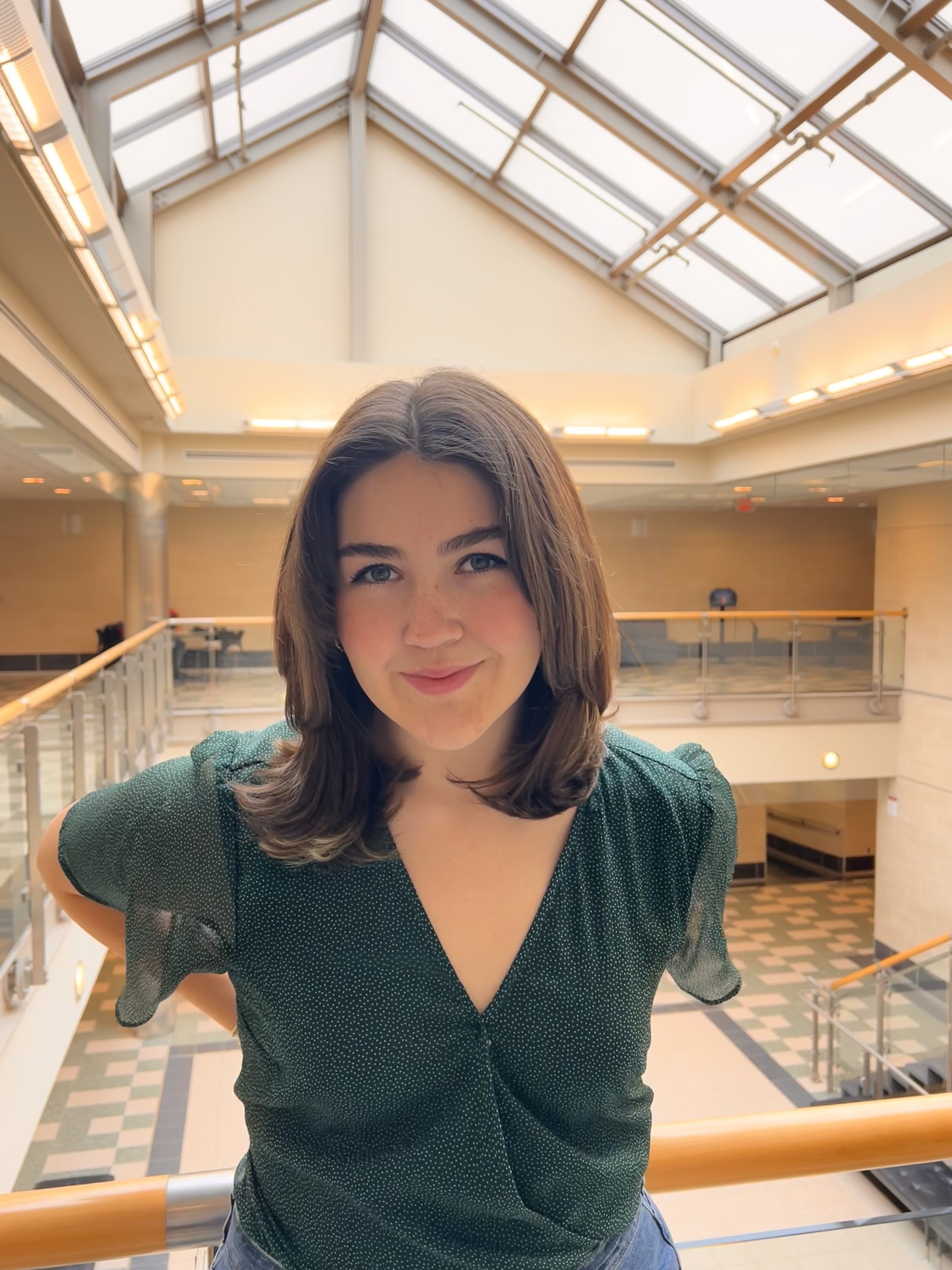 Laci Burton Person smiling for the camera inside a brightly lit atrium with a glass ceiling and railing.